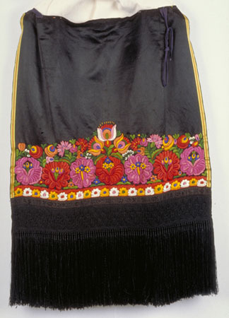 Satin and cotton apron with a multi-coloured embroidered floral motif. The bottom part of the apron is richly decorated with black lace and a long fringe. It was made in Hungary around 1920., © CMC/MCC, 76-515.5