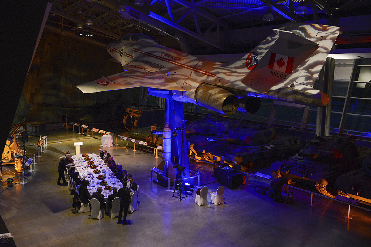 Un groupe de personnes est assise autour d'une table au Musée canadien de la guerre, à Ottawa, avec un avion de chasse.