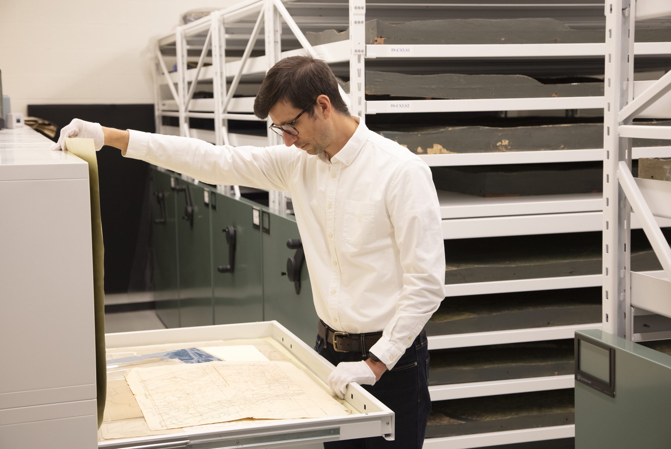 Man opening historical doc in storage with globes