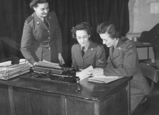 Three women in army uniforms sitting at a desk with a typewriter.